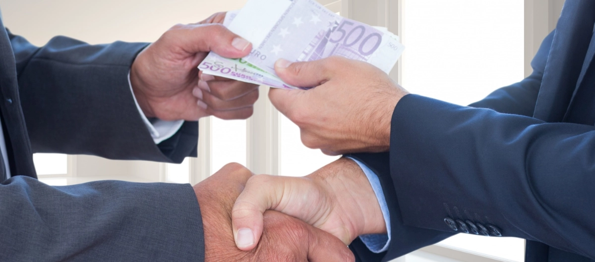 Apretón de manos con intercambio de dinero ilustrando el delito de corrupción en los negocios.